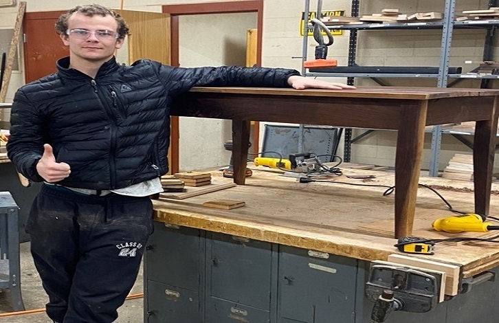 Boy displaying a coffee table he made in woodshop