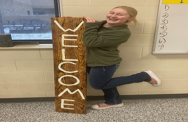 girl displaying her welcome sign she made in woodshop